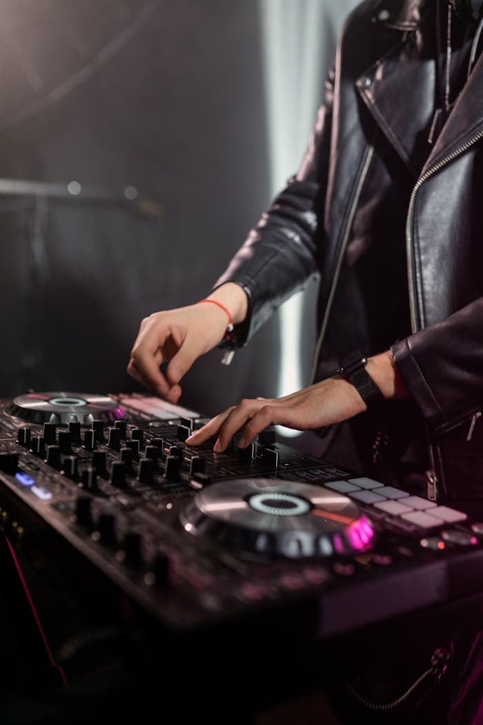 A DJ skillfully mixes music on a DJ mixer while wearing a leather jacket.